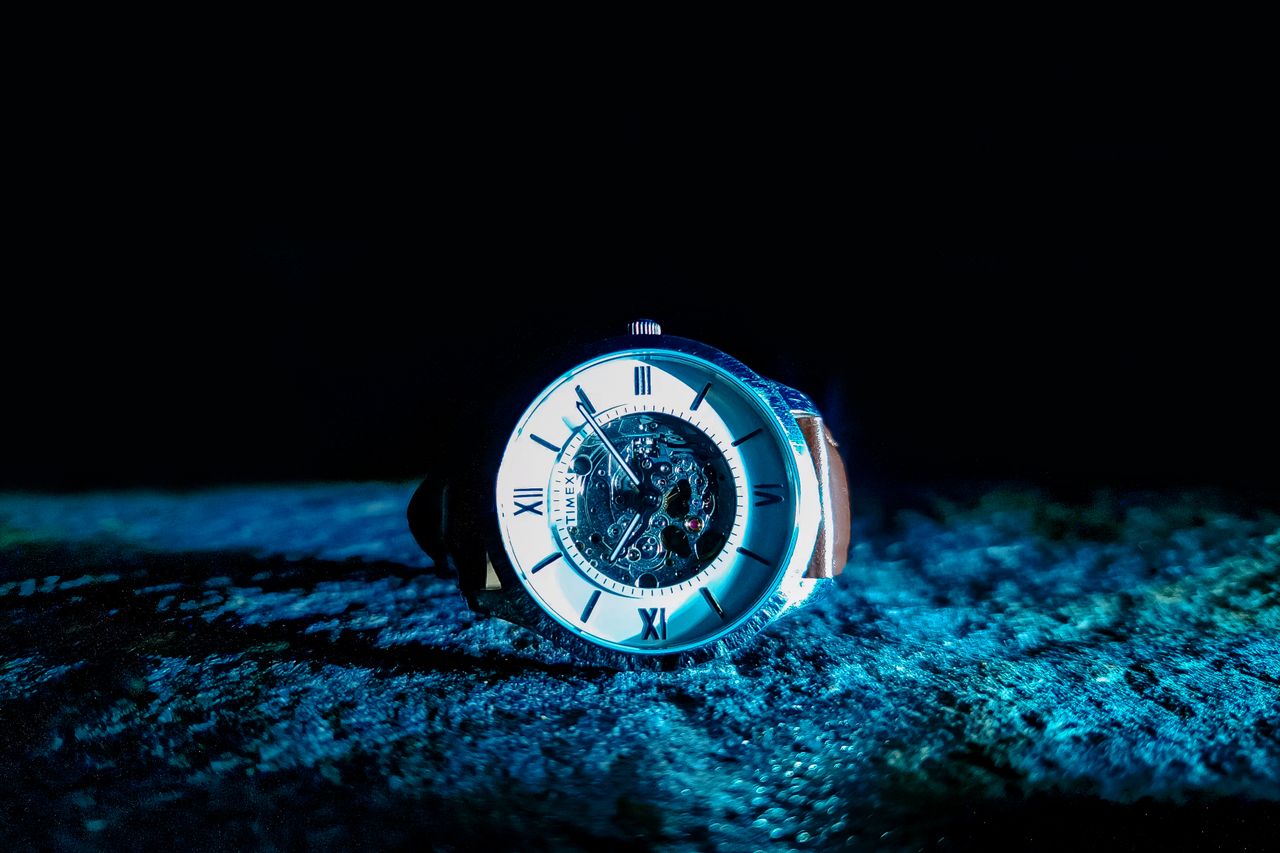 services-01 Close-up of a mechanical watch with Roman numerals, illuminated in dramatic lighting.