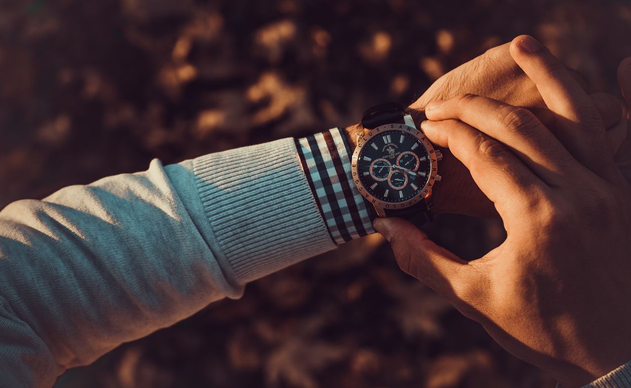 Close-up of a luxury wristwatch on a man's wrist, touched by another hand, in a warm autumn setting.